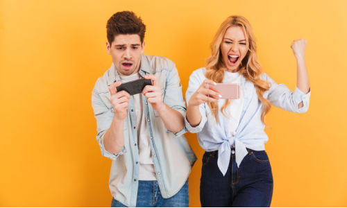 man and woman playing games on their mobile devices rejoicing over online casino real money wins