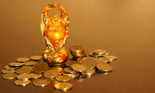 A small laughing Buddha statue with gold coins on golden background