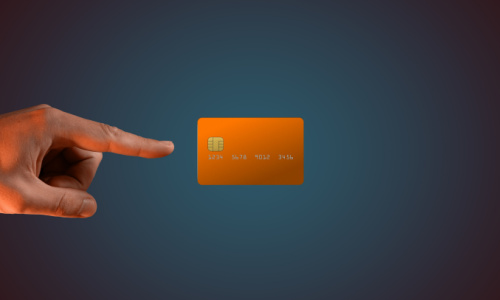 A male hand pointing towards an orange bank card on a dark background