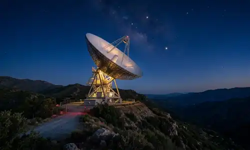 A photograph of a large radio telescope dish on a hillside against a deep blue twilight sky background