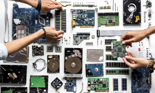 An overhead view hands on either side of computer parts on a white surface 