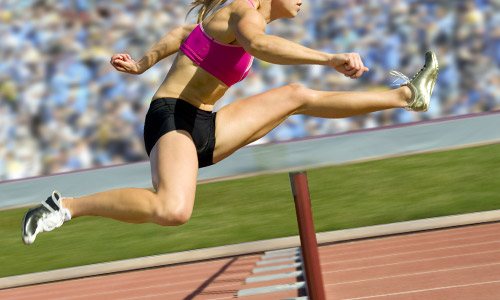 a woman athlete jumping a hurdle 
